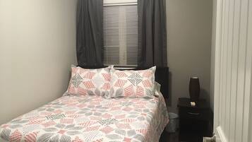 A bedroom with a bed, a window with curtains, a bedside table with a vase, and a door.