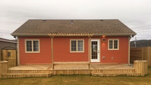 Een rode woning met een veranda, een garage en een omheinde tuin.