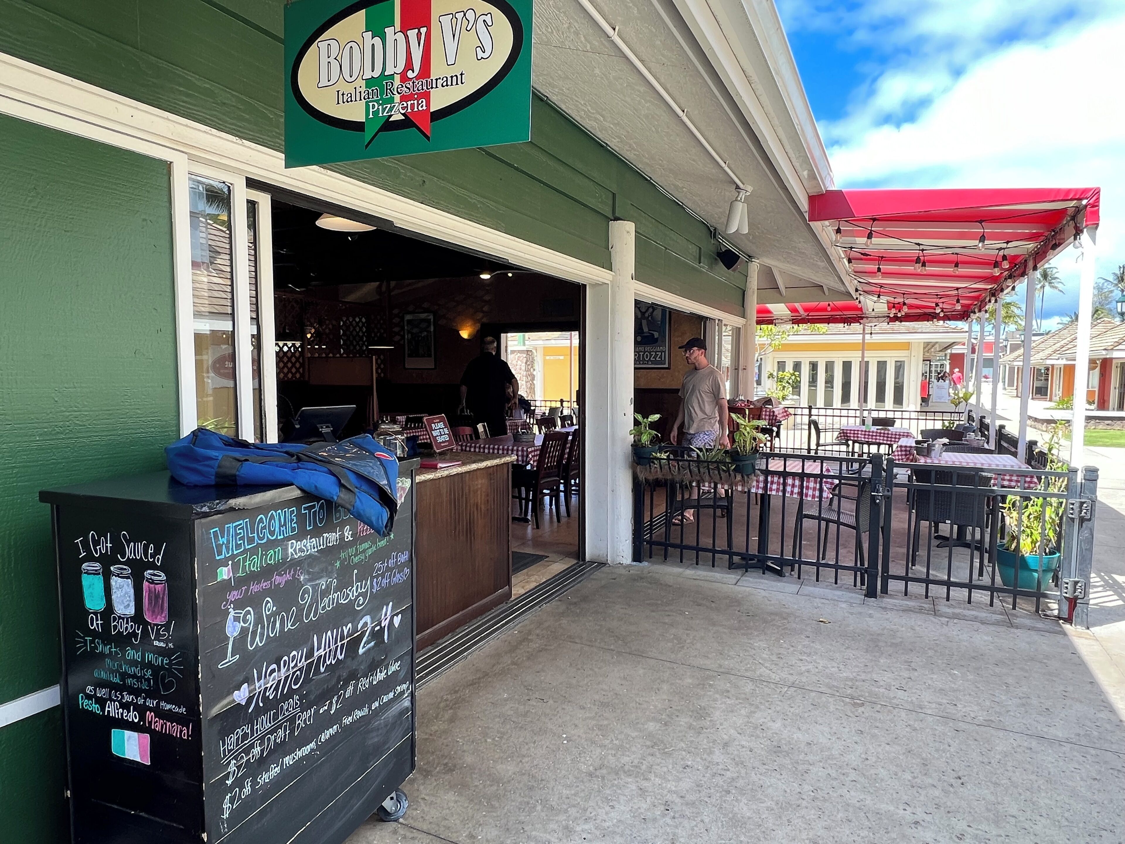 An Italian restaurant with outdoor seating, a chalkboard menu, and a sign indicating a special offer on draft beer.