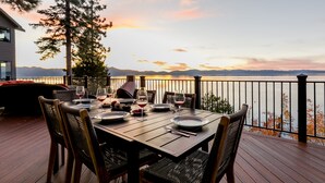 A wooden deck with a table set for dining, overlooking a body of water and mountains. -  Beautiful Lakefront Home with Pier and Buoy. (Glenbrook)