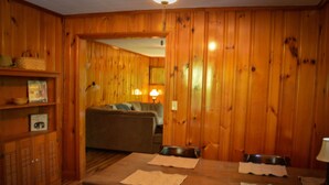 Una habitación con paneles de madera, una mesa de comedor, sillas y un sofá al fondo.