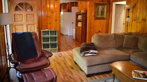 Un salón con paneles de madera, un sillón de cuero, un sofá, una mesa de centro y una estantería.
