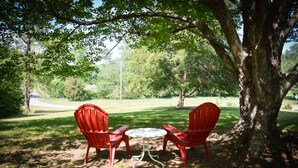 Un parque con dos sillas rojas y una mesa pequeña bajo un árbol.