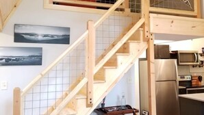 A wooden staircase with a glass railing, a kitchen area with a refrigerator and microwave, and a dining table with chairs. - A-Frame Cabin Escape in George Washington Natl Forest, Lost River Area, WV (Wardensville)