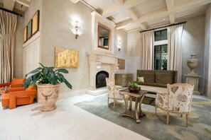 Una sala de estar con chimenea, un sofá naranja, sillones estampados y una planta grande en maceta.