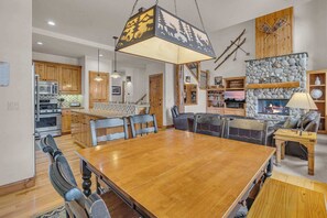 Un vaste espace de vie comprenant une grande table à manger en bois, une cheminée et une cuisine située à l’arrière-plan.