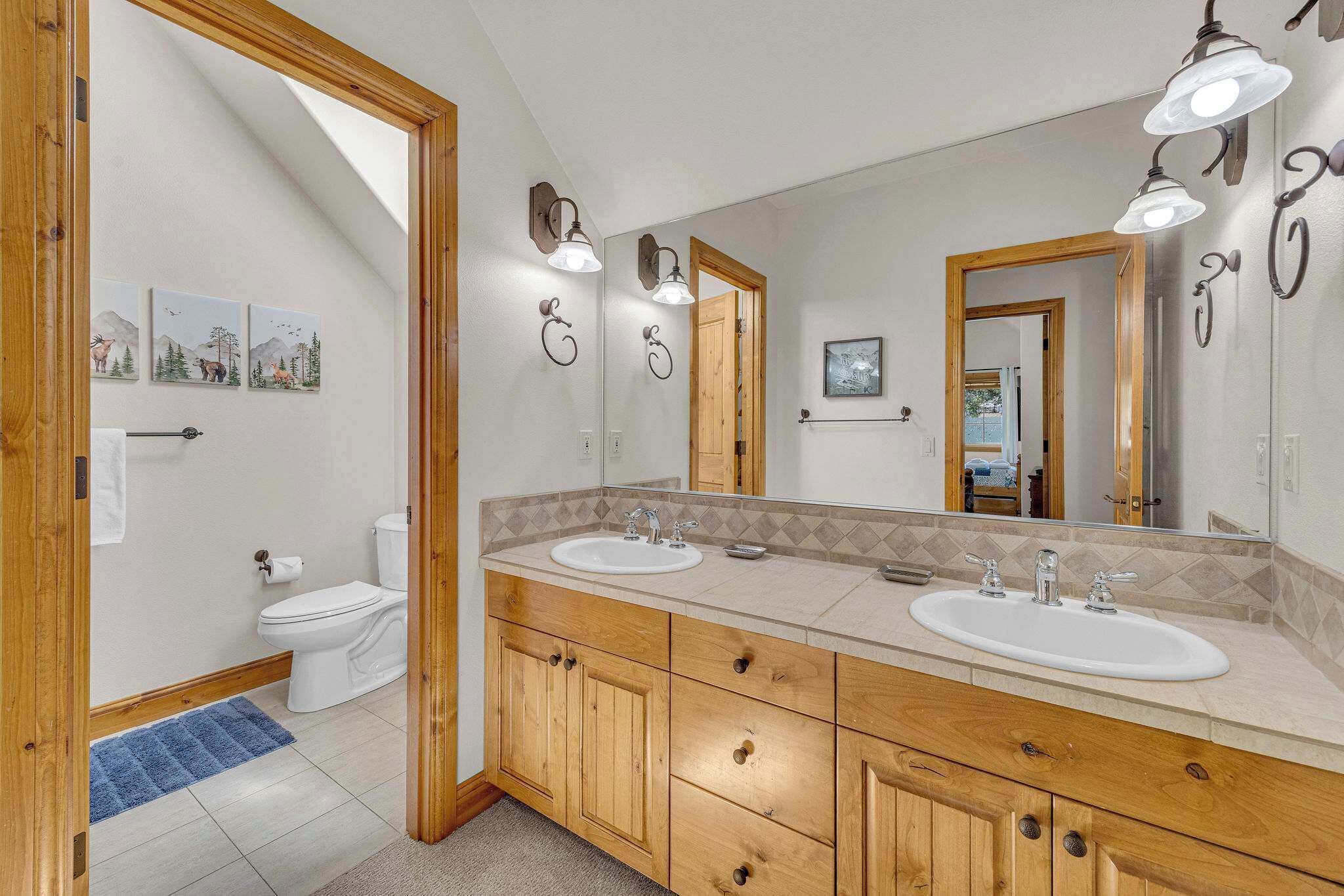 A bathroom with two sinks, wooden cabinets, a large mirror, and wall-mounted lights.