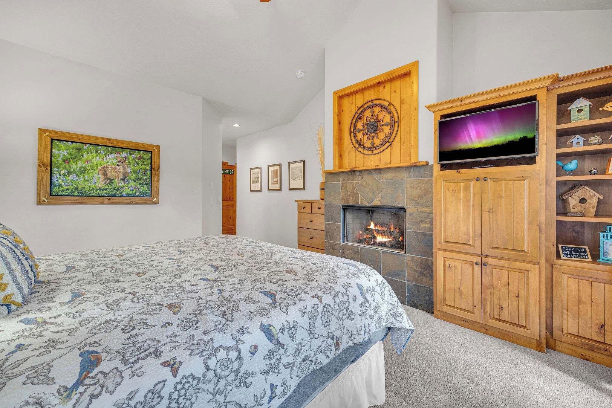 A bedroom with a bed, a fireplace, a TV, and a wooden cabinet with birdhouses.