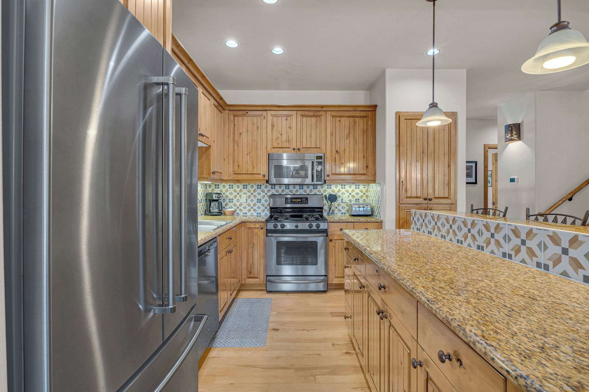 A kitchen with wooden cabinets, stainless steel appliances, a granite countertop, and pendant lighting.