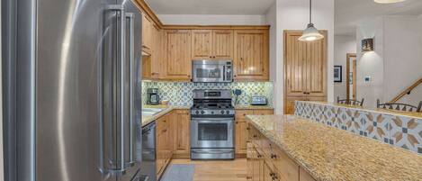 A kitchen with wooden cabinets, stainless steel appliances, a granite countertop, and pendant lighting.