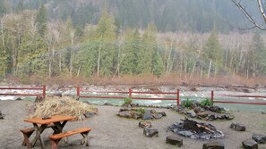Un área de picnic con banco y mesa, una fogata y vistas a un río y bosque.