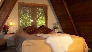 A cozy bedroom with a sloped ceiling, a bed with a white blanket, and a window with curtains.