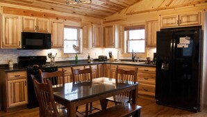 Una cocina amplia con armarios de madera, una mesa de comedor con sillas, un refrigerador negro y una araña.