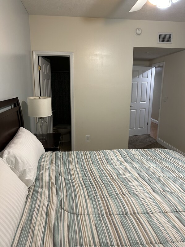 Un dormitorio con una cama, una mesita de noche, una lámpara y una puerta que da a otra habitación.