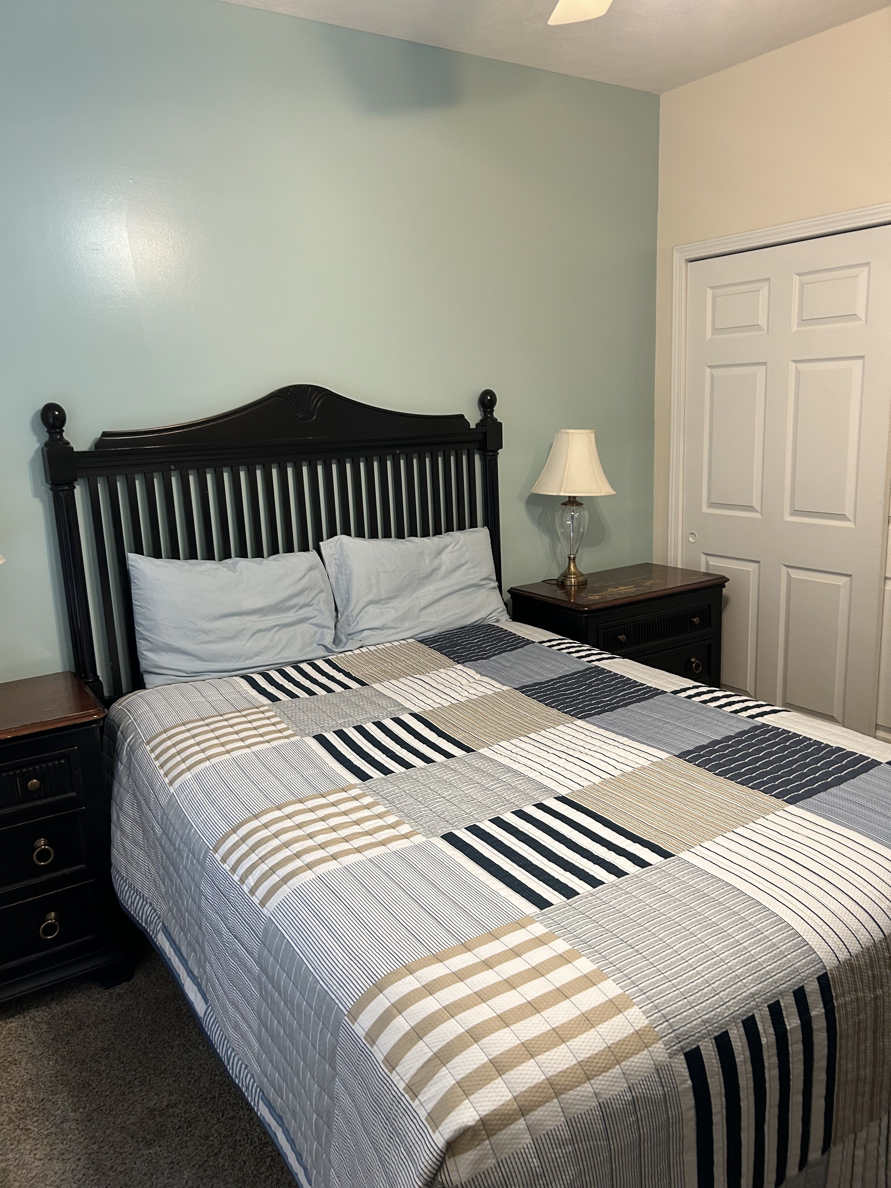 A neatly made bed with a striped quilt, a wooden headboard, and a bedside table with a lamp.