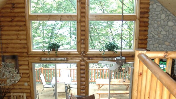 A cabin interior with a large central window, wooden walls, a dining area, and a view of the outdoors.