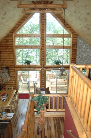 Interior de una cabaña con un ventanal grande, paredes de madera, un comedor y vistas al exterior.
