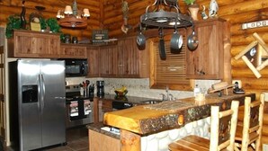 A rustic kitchen with wooden cabinets, a stainless steel refrigerator, hanging pots, and a wooden island with stools.