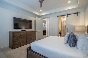 Ein Schlafzimmer mit Bett, Schminktisch, Fernseher und einer Schiebetür zu einem Badezimmer.
