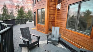 A wooden deck with outdoor furniture, including chairs and a table, and a large window on the building. - RETREAT TO A SECLUDED, SERENE MOUNTAIN LODGE (Bethel)