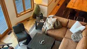A cozy living room with a sectional sofa, a coffee table, and a small side table. There is a window with blinds, a lamp, and a potted plant. - RETREAT TO A SECLUDED, SERENE MOUNTAIN LODGE (Bethel)