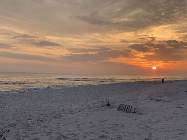 Une plage au coucher du soleil, avec des vagues et des empreintes de pas.