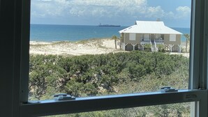 Ett hus vid stranden med utsikt över havet och ett fartyg i fjärran.
