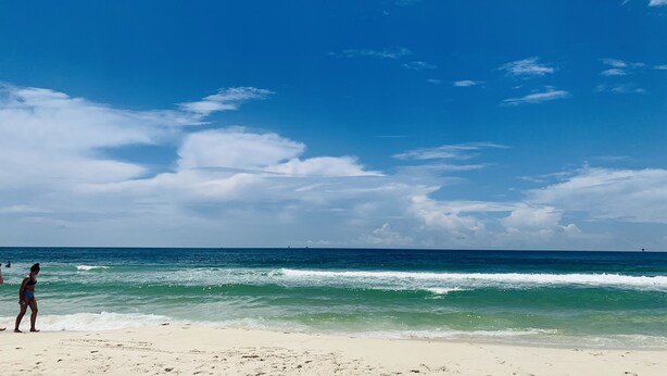 En strand med klar himmel och vågor som rullar in mot land.