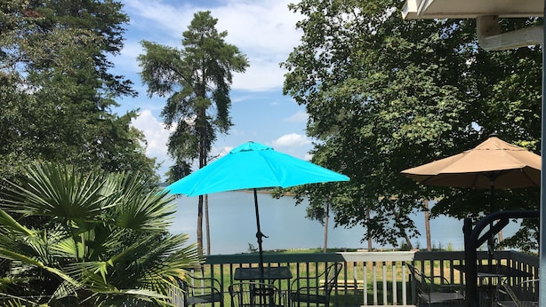 An outdoor deck with a view of a lake, surrounded by trees and equipped with outdoor furniture. - Lakehouse Retreat with dock, paddle boat, canoe & kayaks! Now have Gas Grill  (Anderson)