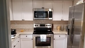 A compact kitchen with white cabinets, a stainless steel microwave, oven, and refrigerator. - Centrally located Oasis  (Sarasota)