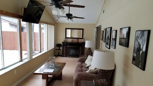 A living room with a sofa, coffee table, and a fireplace. There are ceiling fans, a TV, and framed pictures on the wall. - Centrally located Oasis  (Sarasota)