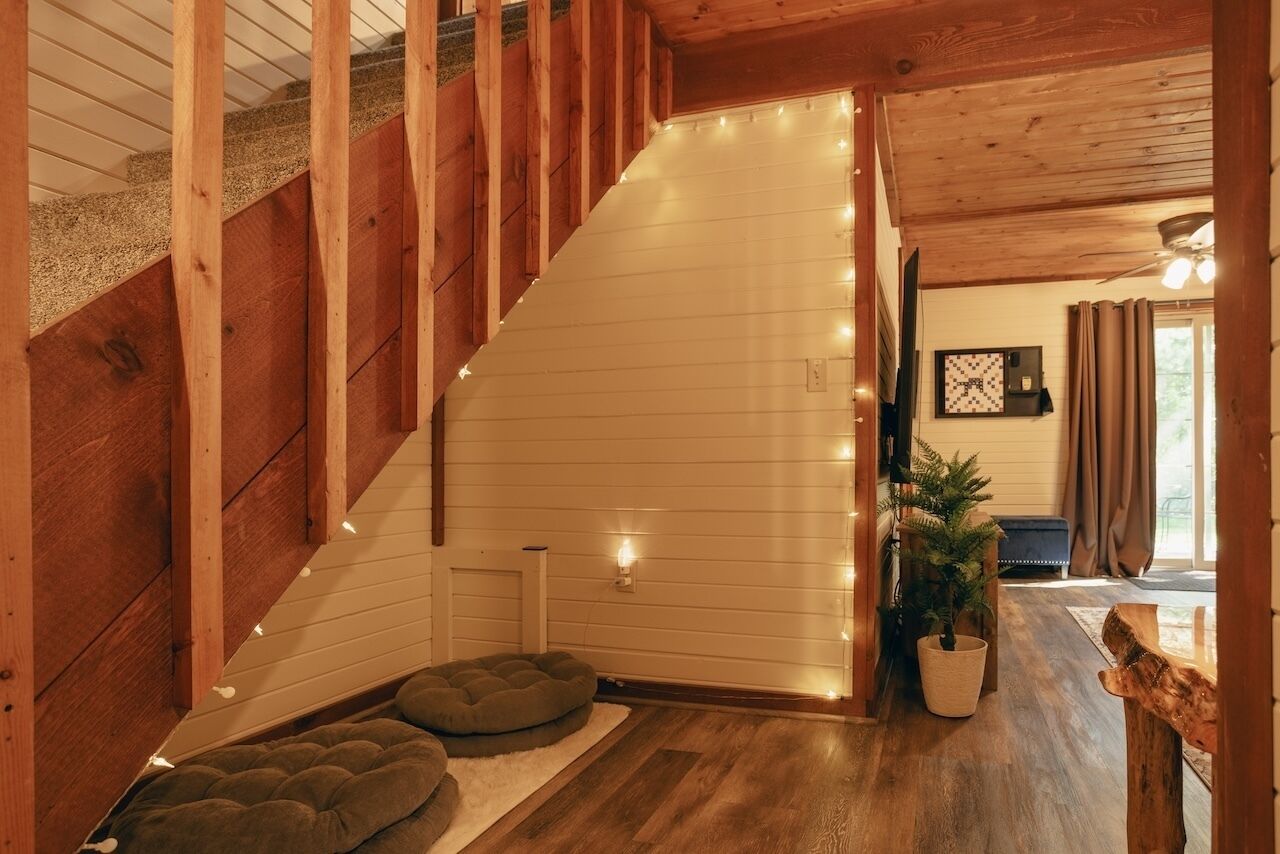 Un escalier en bois mène à une pièce dont le mur est blanc, où se trouvent une petite table blanche, un coussin vert et une plante en pot.