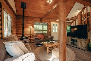 A log cabin interior with a sofa, a coffee table, a fireplace, a television, and a staircase.