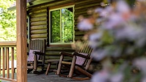 Une cabane en rondins avec une véranda, deux fauteuils à bascule et une fenêtre.