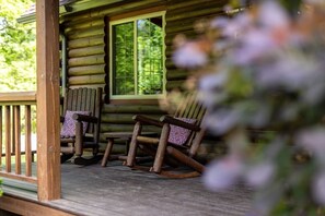 Une cabane en rondins avec une véranda, deux fauteuils à bascule et une fenêtre.