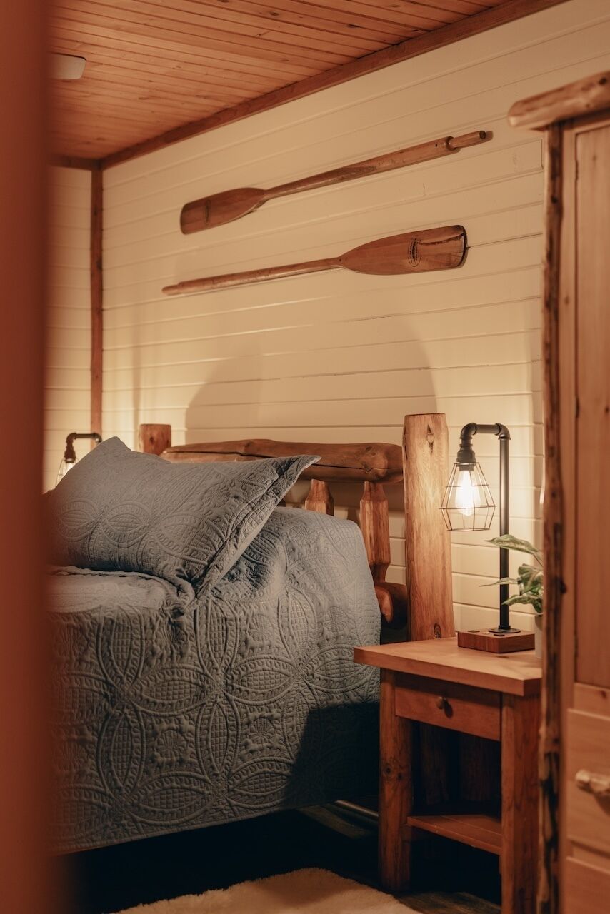 Ein gemütliches Zimmer mit einem hölzernen Bett, einem Nachttisch mit Lampe und an der Wand aufgehängten Holzschlägern.