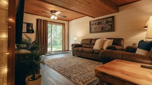 Un salon chaleureux avec un plafond en bois, un canapé en cuir marron, un tapis à motifs et un ventilateur de plafond.