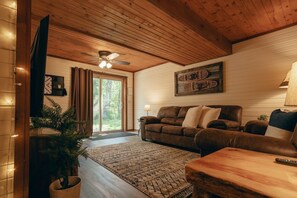 Ein gemütliches Wohnzimmer mit Holzbalkendecke, einem braunen Ledersofa, einem gemusterten Teppich und einem Deckenventilator.