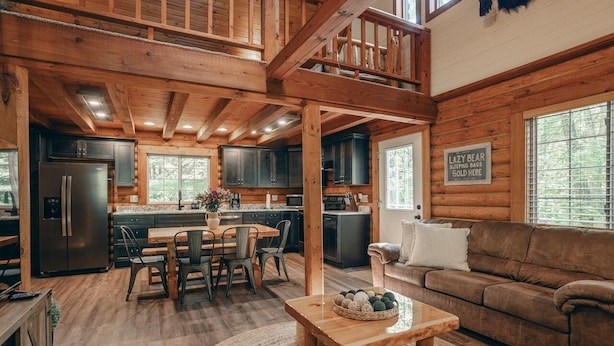 Un intérieur de cabine spacieux comprenant une cuisine, un coin repas et un salon, avec des poutres en bois et de grandes fenêtres.