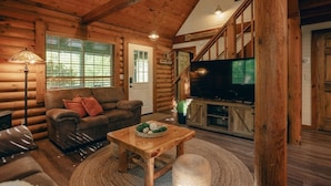 L’intérieur d’une cabane en rondins, avec un plafond en bois, un canapé, un téléviseur et un escalier.