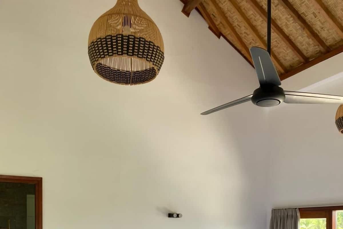 Een slaapkamer met een groot bed, een plafondventilator en een geweven lamp.