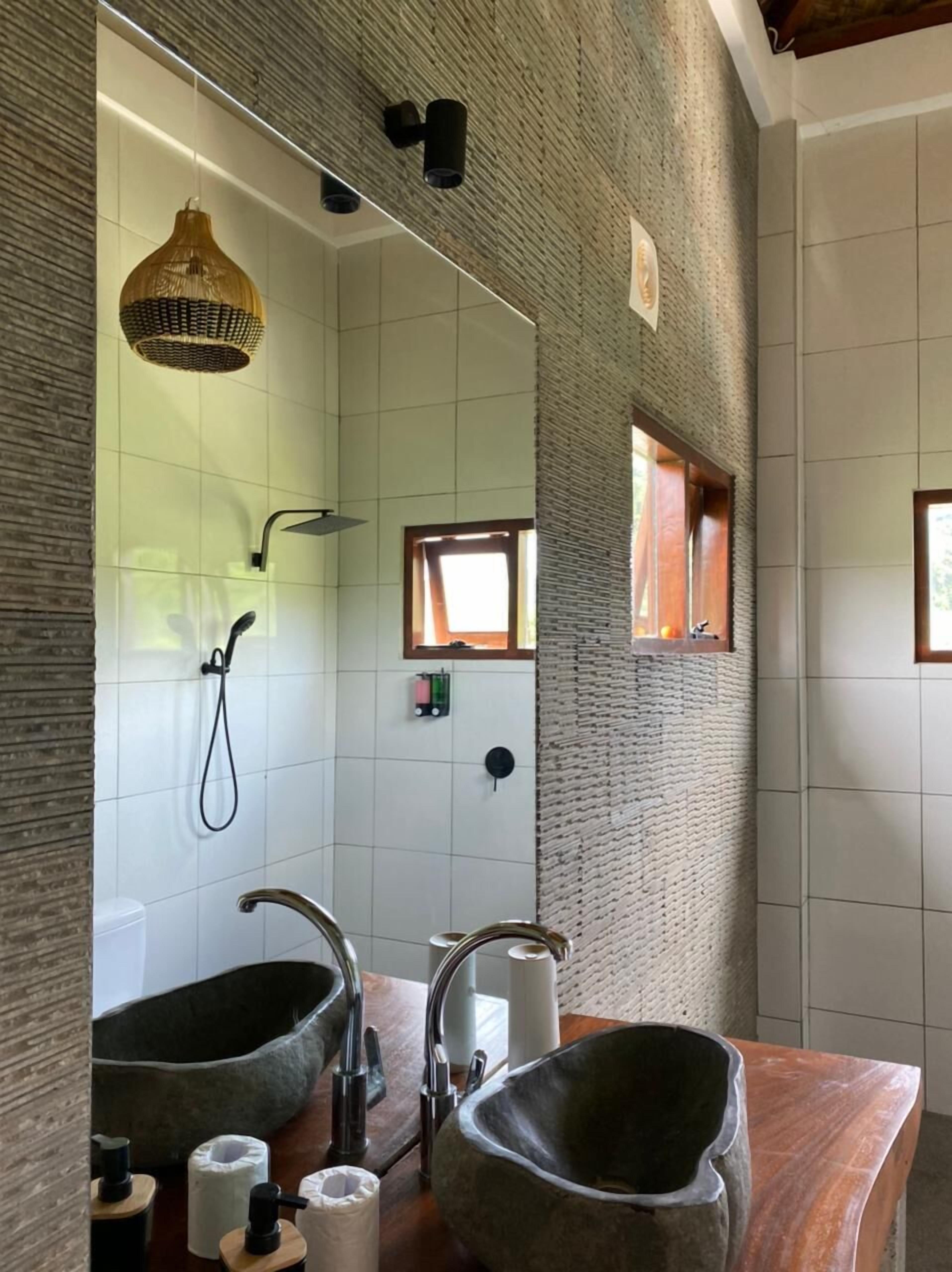 Un bagno con due lavabi in pietra, uno specchio grande, una doccia con soffione estraibile e un muro a rilievo.