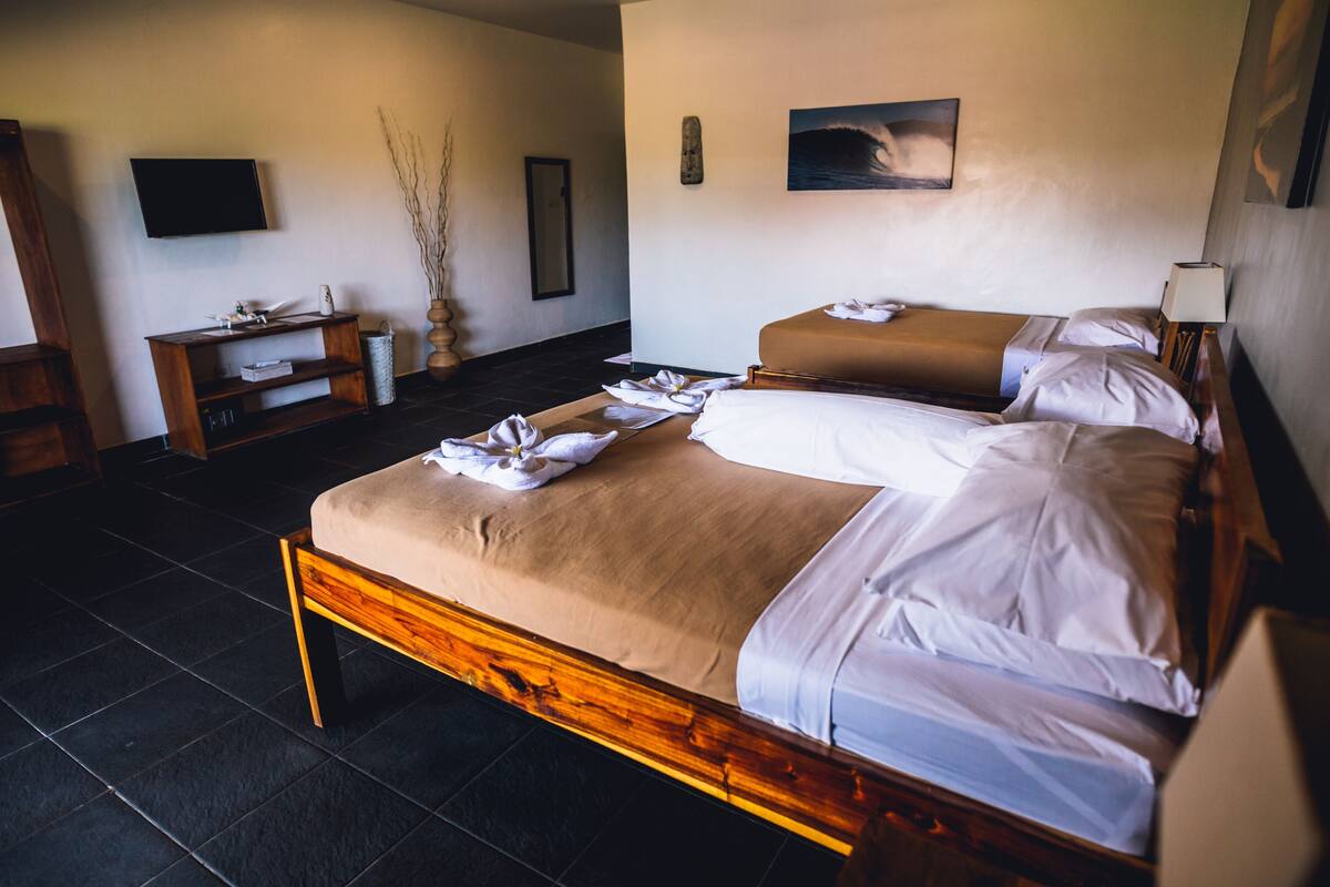 Een hotelkamer met twee bedden, een flatscreen televisie, een houten bankje en een aan de muur hangend schilderij.