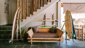 A bamboo staircase with surfboards leaning against it, a bamboo sofa with cushions, and a dining area with wooden furniture. - Baha Baha Villas (Sumbawa Barat)