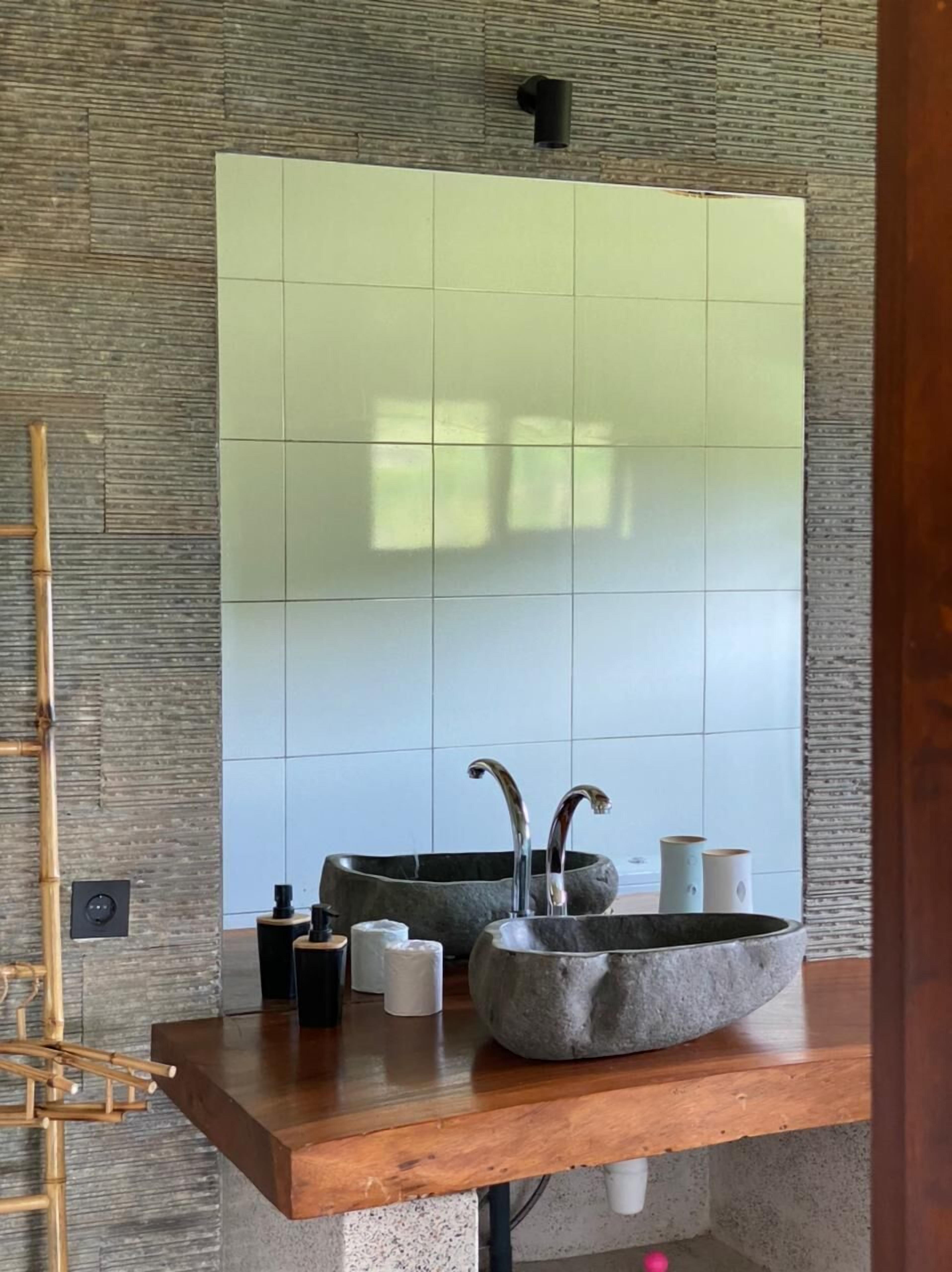 A bathroom with a large mirror, a stone sink, and a bamboo shelf.