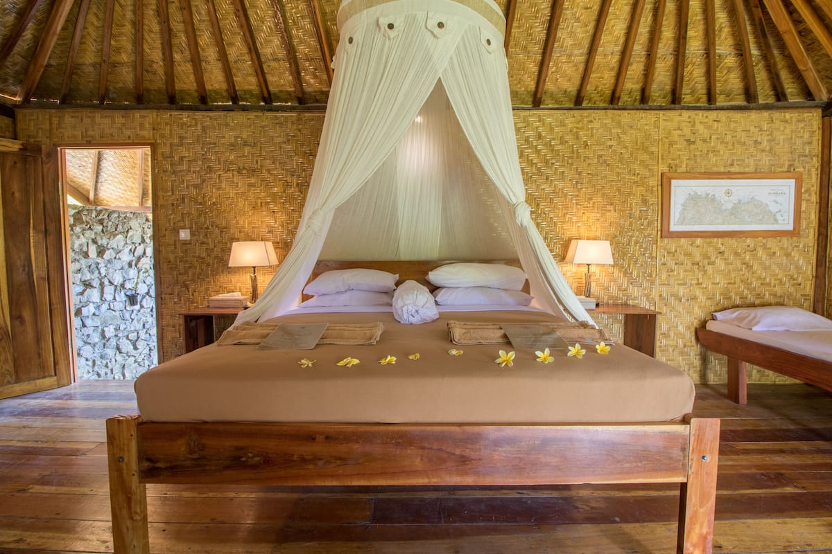 Een houten bed met hemel, twee nachtkastjes en een stenen muur.