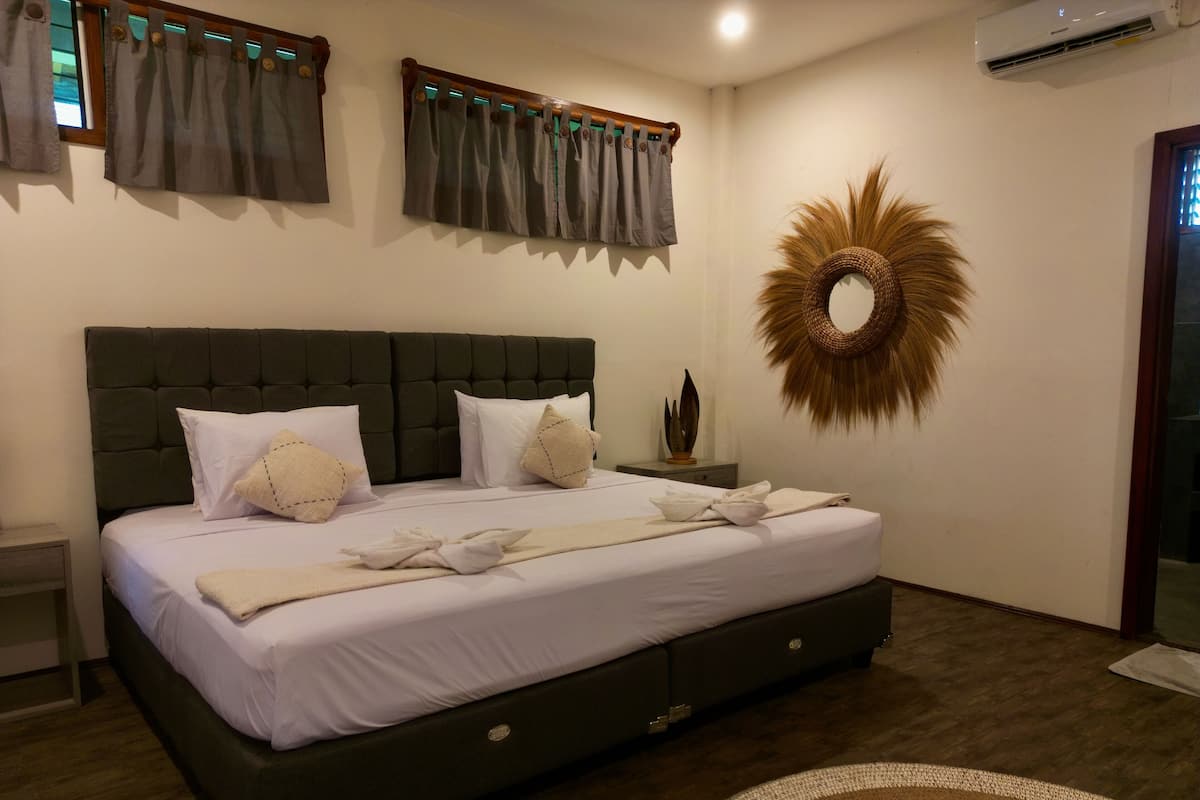 Een slaapkamer met een groot bed, een donker hoofdbord, wit beddengoed en een decoratief wandobject.