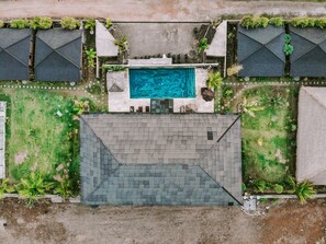 Vue aérienne d’une propriété dotée d’une piscine centrale, entourée de pelouses verdoyantes et de quelques arbres.