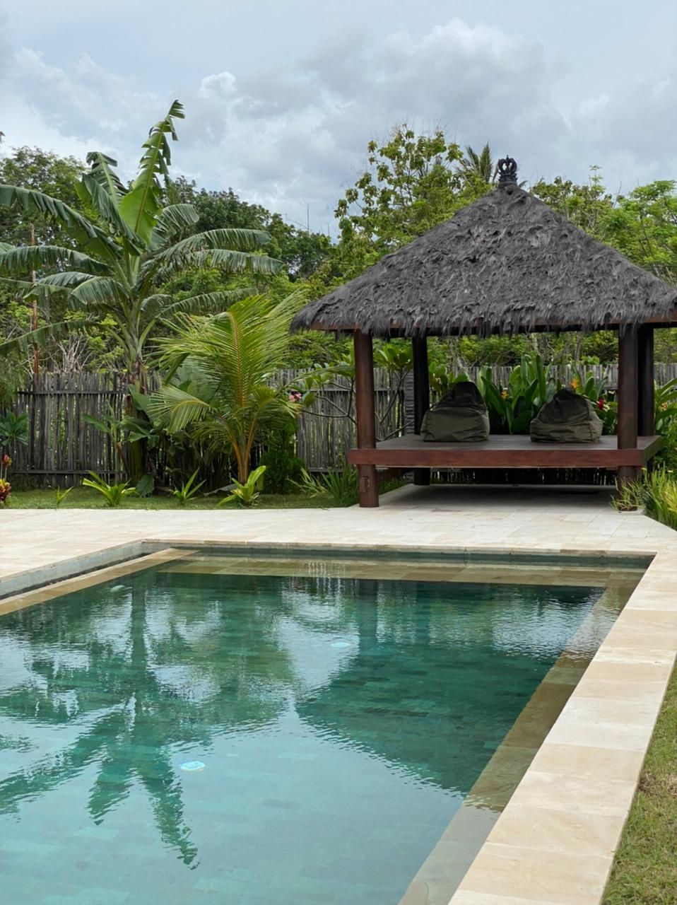 A pool with a thatched-roof gazebo, surrounded by tropical vegetation.