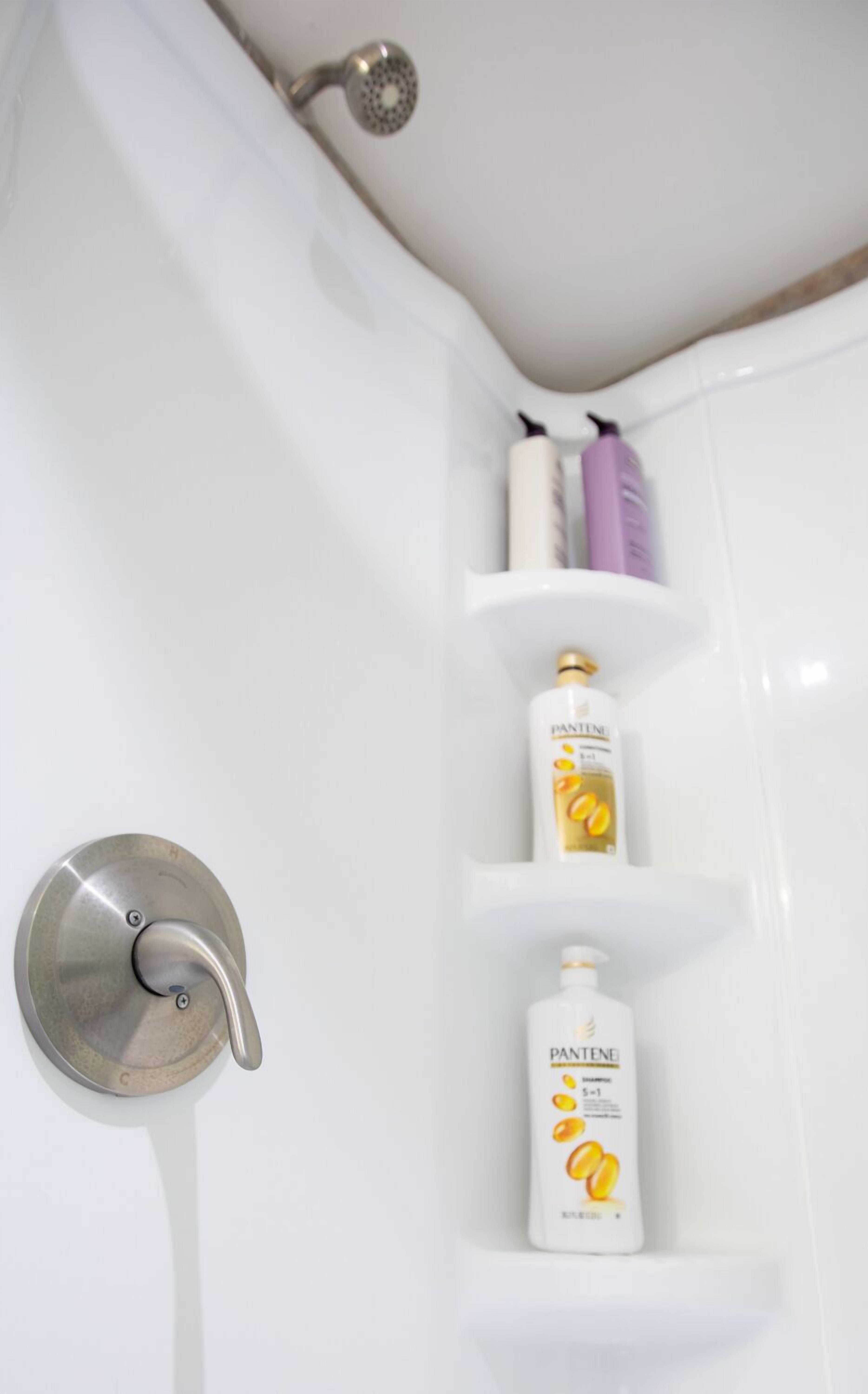 A bathroom with a shower curtain, a handheld showerhead, and two Pantene shampoo bottles on a shelf.